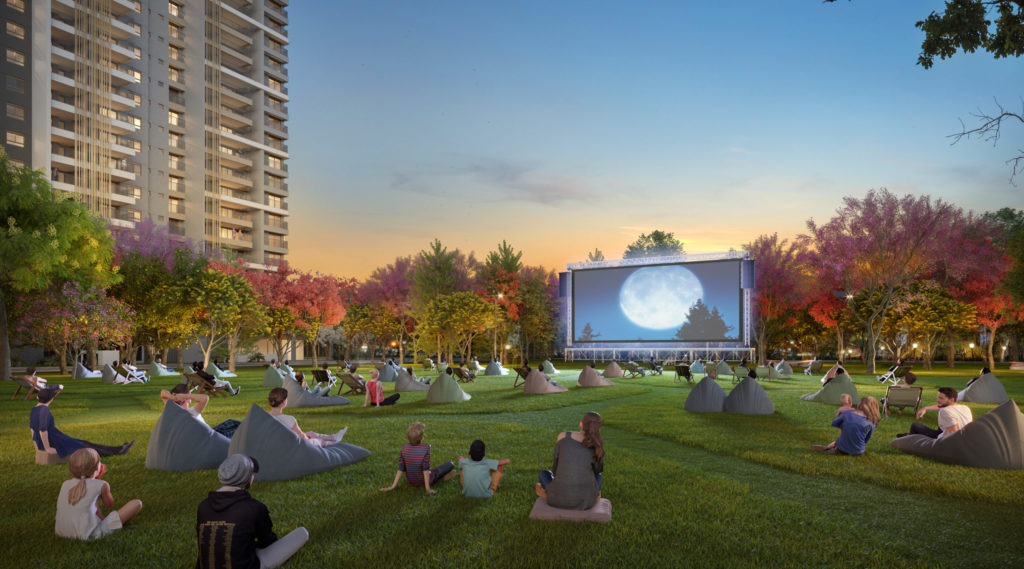 Famílias assistem a filme ao ar livre na Praça do ÉDEN Brooklin Park by Dror, cercadas por área verde e árvores floridas