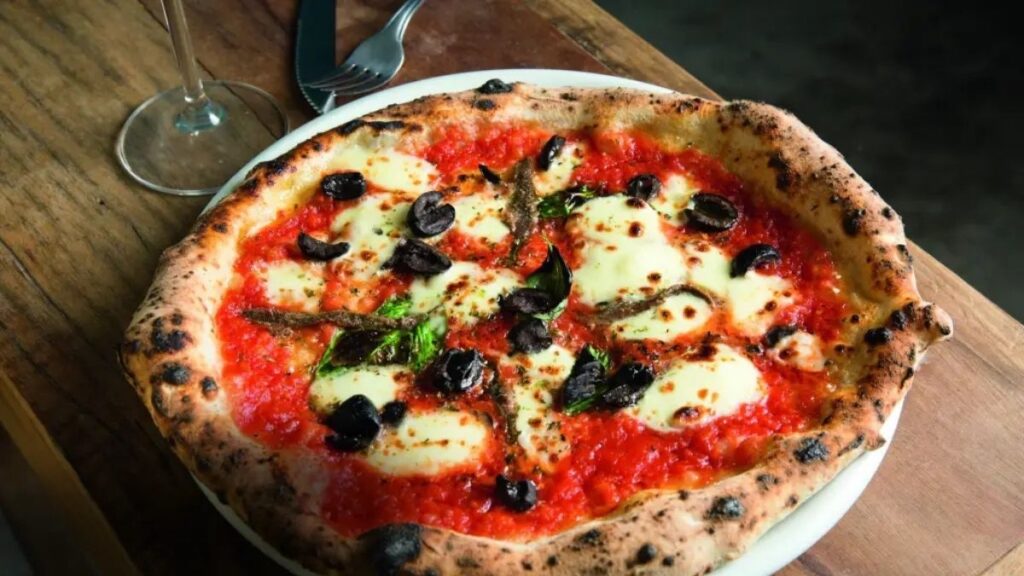 🍕Dia Mundial Da Pizza: Confira As 3 Melhores Pizzarias De Pinheiros Em 2025 4 Pizza Napolitana Da Leggera Com Borda Alta, Molho De Tomate, Mussarela, Azeitonas E Aliche Sobre Mesa Rústica